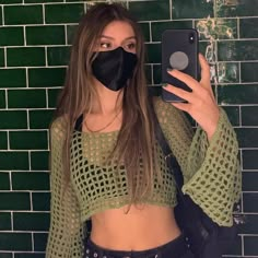 a woman wearing a black mask and holding a cell phone in front of a green brick wall