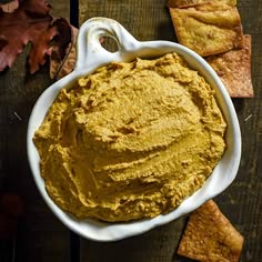 a white bowl filled with hummus next to crackers on top of a wooden table