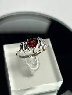 1 x Beautiful .925 Silver Adjustable Devilish Bat Wing Ring With A Prong Set Heart Shaped Garnet Crystal Gemstone - Supplied With Gift Box. Bat Wings & Devilish Horns Design With Gold Plated on 925 Silver Devil Tail Detail. Crystal Measures Approx 5mm x 6.6mm Total Design Measures 15.6mm x 10.4mm  Adjustable at the back of the ring so can be expanded or reduced in size. One side of the ring is thinner than the other side, this is because it has to slot into the thicker side to allow it to be adjustable. Please be gentle when adjusting the ring as it can cause the ring to mis-shape if you are too rough with it. Please note that silver can oxidise over time, it just needs cleaning with a silver cleaning cloth. The item is sent with an anti tarnish strip for safety whilst in transit. I will p Horns Design, Bat Ring, Wing Ring, Garnet Heart, Garnet Crystal, Garnet Gem, Hippy Gifts, Bat Wing, Halloween Desserts