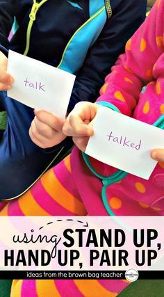 two children sitting on the ground holding up paper with words that read, using stand up, handup, pair up