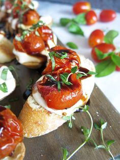 several small sandwiches with tomatoes and sauce on them sitting on a cutting board next to fresh basil