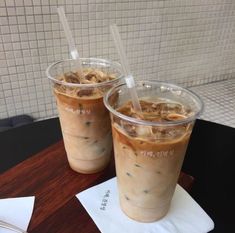 two iced coffees sitting on top of a wooden table