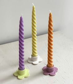 three candles sitting on top of each other in the shape of flower vases, one yellow and one purple