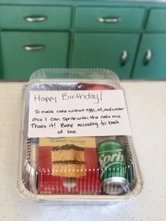 a birthday card in a plastic container on top of a counter with sodas and cookies