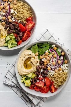 two bowls filled with different types of salads on top of a white wooden table