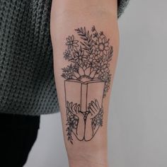 a woman with a tattoo on her arm is holding a book and flowers in it