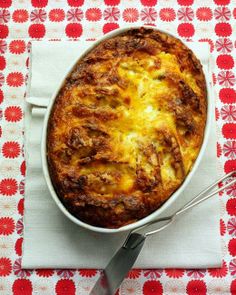 a casserole on a red and white tablecloth with utensils next to it