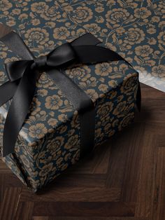 a blue and gold gift box with a black bow on it's side sitting on a wood floor