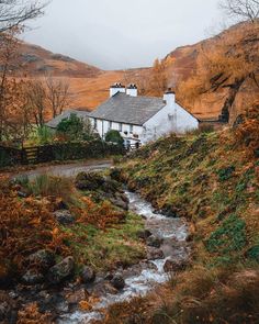 a small white house sitting on top of a lush green hillside next to a river