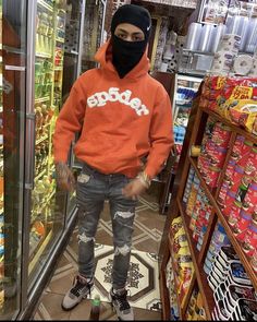 a young man wearing an orange hoodie standing in front of a store filled with food