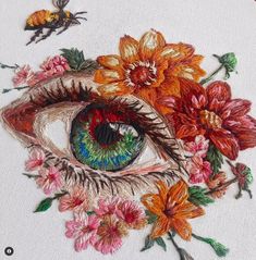 an eye surrounded by flowers and bees on a white cloth with red, orange, yellow and green colors