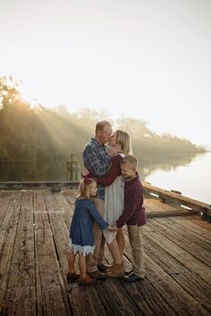 a family standing on a dock with the sun shining through the trees in the background