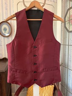 This handsome vest is burgundy with a black sheen/shift on one side and solid black on the other side! It has the original buttons, with three outer pockets on the burgundy side (two of them haven't been opened/unstitched yet) and one chest pocket on the black side. The measurements, taken with the vest lying flat, are: shoulder to shoulder, 12 inches; armpit to armpit, 19 inches; length, 25 1/2 inches in front and 22 inches in back; bottom edge, 17 1/2 inches. In very good condition. Burgundy Vest Outfit Men, Maroon Vest Outfit Men, Classic Sleeveless Solid Outerwear, Sleeveless Business Vest Outerwear, Formal Winter Sleeveless Vest, Fitted Sleeveless Vest With Pockets, Sleeveless Formal Winter Outerwear, Formal Sleeveless Winter Outerwear, Formal Sleeveless Winter Vest