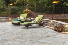 two lounge chairs sitting on top of a patio next to a stone wall and fire pit