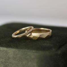 two gold wedding rings sitting on top of a green cloth