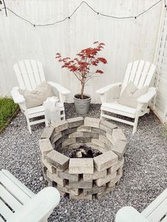 an outdoor fire pit surrounded by chairs and a pot with a tree in it on gravel