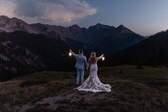 a bride and groom standing on top of a mountain holding torches in their hands as the sun sets