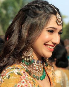 a woman with long hair wearing jewelry and smiling at the camera while standing in front of other people