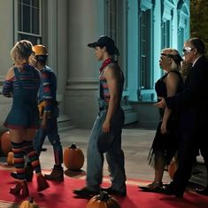 a group of people standing on top of a red carpet next to two pumpkins