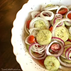 a white bowl filled with onions, cucumbers and tomato slices on top of a wooden table