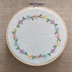 a white cross stitched circle with colorful flowers in the center on a beige background