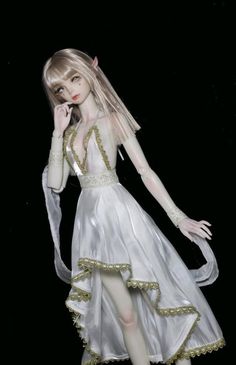 a doll dressed in white and gold is standing on a black background with her hands to her face