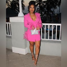 a woman in a bright pink outfit standing on a balcony with palm trees behind her