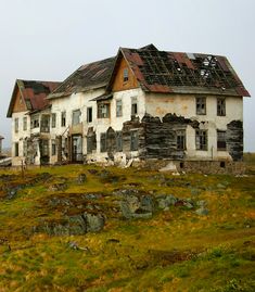 an old house sitting on the side of a hill with grass and rocks around it