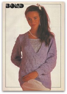 a woman wearing a purple sweater and white pants with her hands on her hips, posing for the camera