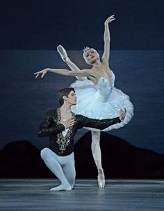 two ballerinas in white tutus and black leotards, one holding the other's leg