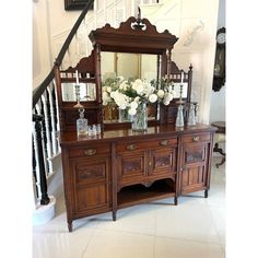 an ornate wooden dresser with flowers and vases on it in front of a staircase