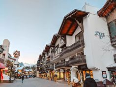 people are walking down the street in front of some shops and buildings with snow capped mountains in the background