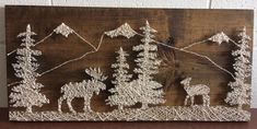 a wooden sign with string art depicting trees and animals in front of a mountain range