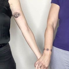 two people holding hands with tattoos on their arms and one is wearing a black dress