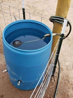 a large blue barrel sitting next to a wooden pole in the dirt near a fence