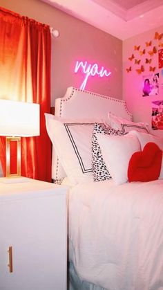 a white bed topped with pillows next to a night stand and red curtains in a bedroom