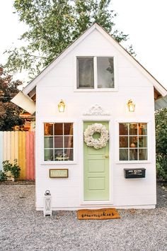 a small white house with a wreath on the front door and lights hanging from the windows