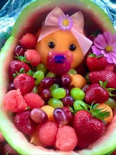 a teddy bear sitting inside of a watermelon bowl filled with grapes and strawberries