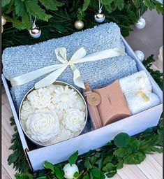 a gift box with white flowers and soaps in it next to a christmas tree