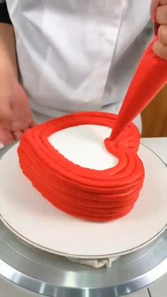 a person is decorating a cake with red icing and rosettes on it