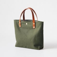 The Green Canvas mini tote is a canvas and leather tote handmade in the KMM & Co. studio in Atlanta. Each one is meticulously crafted from heavyweight canvas and gorgeous full-grain leather. Green Canvas is a type of cotton canvas known as duck cloth. It's one of the most durable types of cloth, and it's structured enough to stand up on its own. The Green Canvas mini tote comes standard with Tan handles. Khaki Leather Bag For Everyday Use, Everyday Khaki Leather Canvas Bag, Everyday Khaki Duck Canvas Bag, Everyday Top Handle Canvas Bag, Canvas Bag With Rolled Handles For Everyday Use, Khaki Canvas Bag With Handles, Khaki Canvas Bag, Everyday Canvas Shoulder Bag With Rolled Handles, Everyday Canvas Bag With Rolled Handles