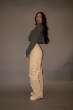 a woman is standing in front of a gray background wearing white pants and a grey sweater