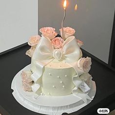 a white cake with pink roses on top and a candle in the middle is sitting on a black table