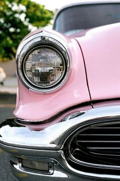 the front end of an old pink car with its headlights turned to show it's chrome