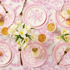 the table is set with pink and white plates, silverware, and flower centerpieces