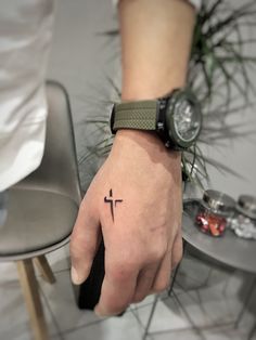 a person's hand with a small cross tattoo on their left thumb and wrist