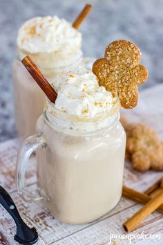 two mugs filled with whipped cream and ginger cookies on a wooden table next to cinnamon sticks