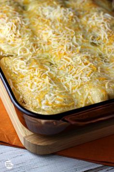 a casserole dish with cheese on top in a wooden tray next to an orange napkin