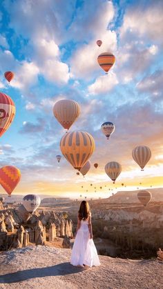 a woman standing on top of a hill surrounded by hot air balloons