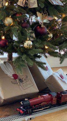 a christmas tree with presents under it and a toy train on the track next to it